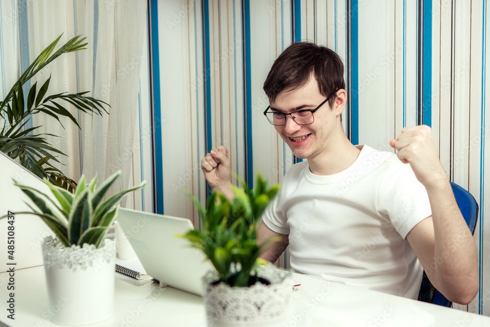 Portrait of a cheerful man, an IT professional working remotely, sitting at a desk and smiling in front of the camera during a break, a human programmer with glasses for vision correction Portrait of a cheerful man, an IT professional working remotely, sitting at a desk and smiling in front of the camera during a break, a human programmer with glasses for vision correction
