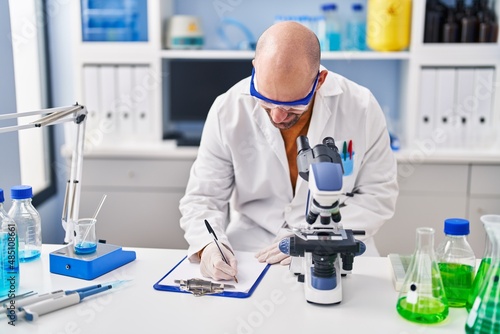Young man scientist writing on clipboard at laboratory