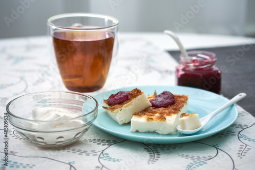 Healthy and tasty breakfast with cottage cheese casserole, sour cream, jam and a cup of tea. Appetising cottage cheese casserole on table, served with jam.