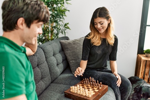 Young caucasian couple smiling happy playing chess game sitting on the sofa with dog at home.