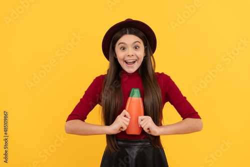 amazed girl in hat hold shampoo. presenting cosmetic product for teen. © Olena