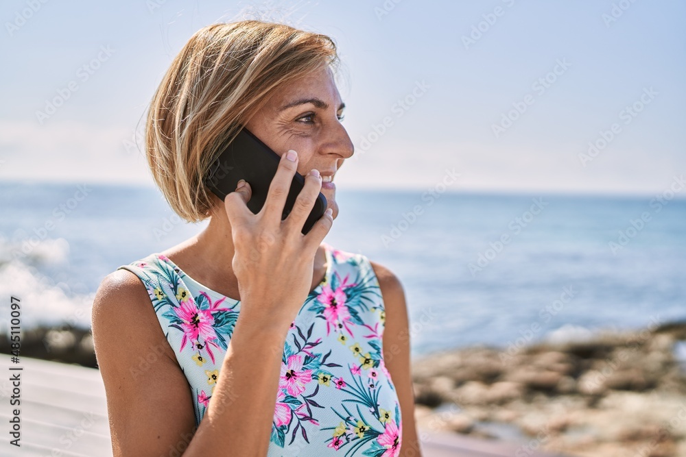 Middle age beautiful woman talking to the phone by the sea