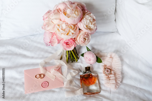 Wedding bride boutonniere, bouquet, perfume and garter laying on white bed linen. Pink bridal flowers and accessories close-up