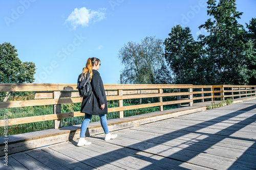a woman tourist with a backpack walks along a wooden bridge in the countryside.
