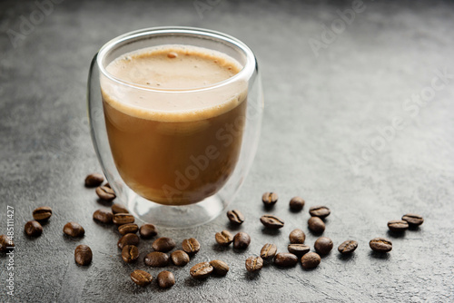 cuppuccino in a double-walled glass cup close-up. A glass of coffee and coffee beans on a dark surface. photo