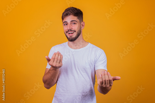young handsome caucasian man wearing white t-shirt against yellow background inviting to come with hand has a warm smile and friendly expression on his face. happy that you came