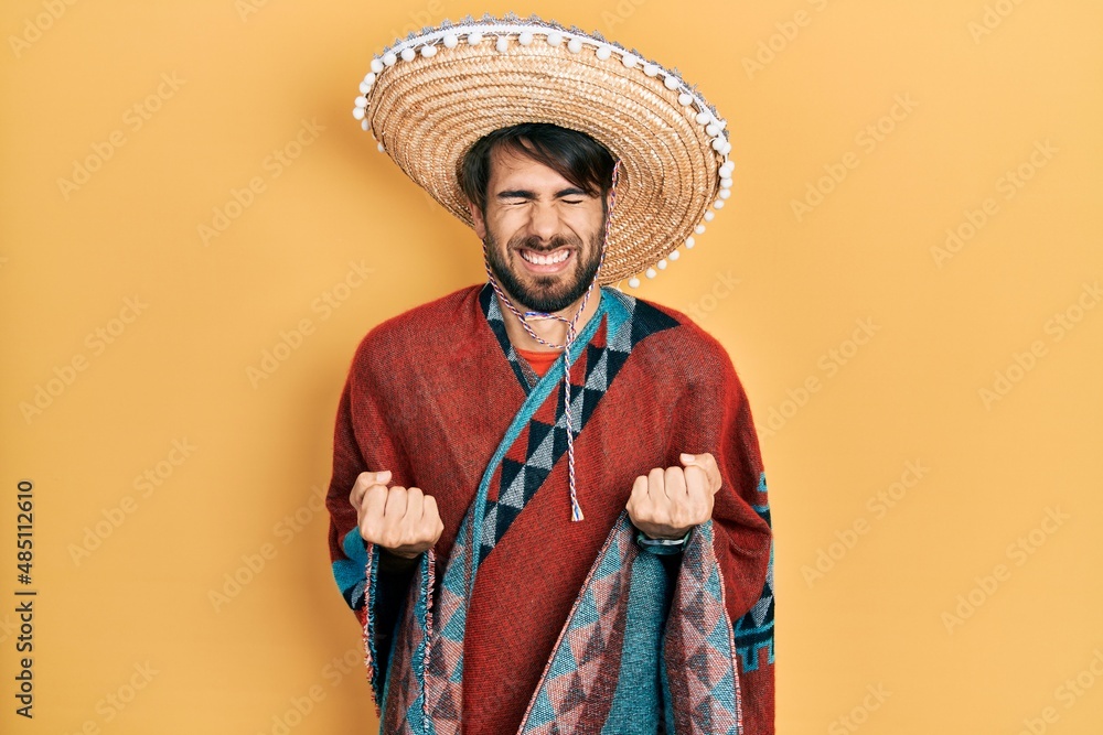 Young hispanic man holding mexican hat excited for success with arms raised and eyes closed celebrating victory smiling. winner concept.