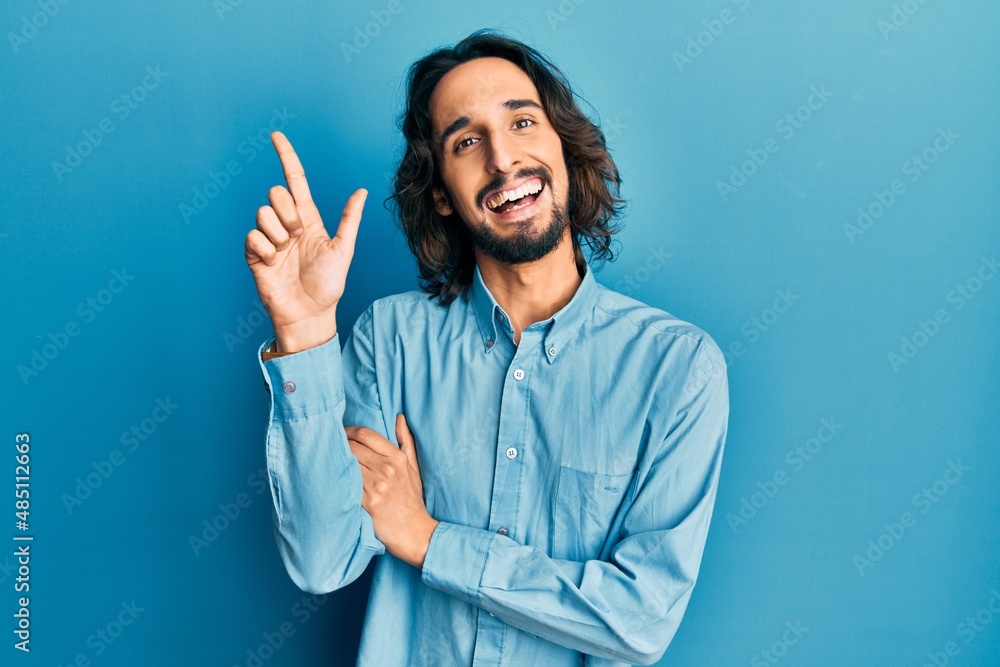Young hispanic man wearing casual clothes with a big smile on face, pointing with hand and finger to the side looking at the camera. Young hispanic man wearing casual clothes with a big smile on face, pointing with hand and finger to the side looking at the camera.