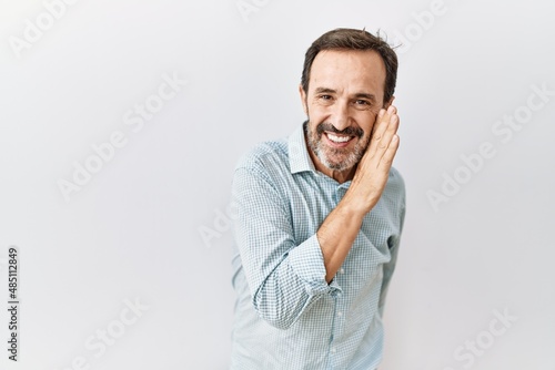 Middle age hispanic man with beard standing over isolated background hand on mouth telling secret rumor, whispering malicious talk conversation