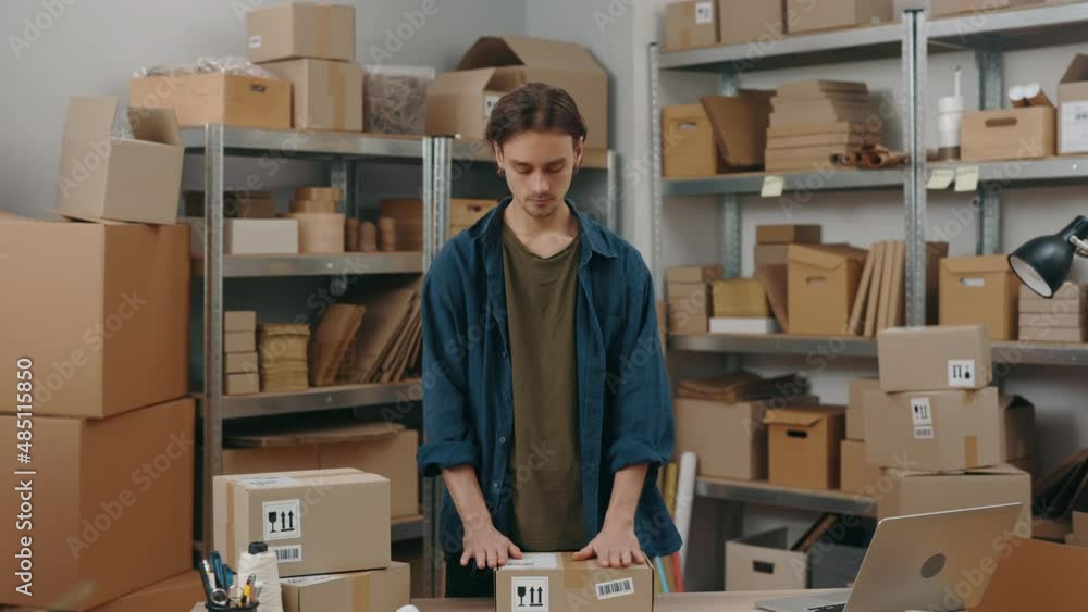 Store owner. Caucasian brunette man putting stickers with client address at the parcel while working at the warehouse. Post service and small business concept. Store owner. Caucasian brunette man putting stickers with client address at the parcel while working at the warehouse. Post service and small business concept.