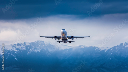 A passenger plane takes off on a cloudy day with snowed mountains in the background