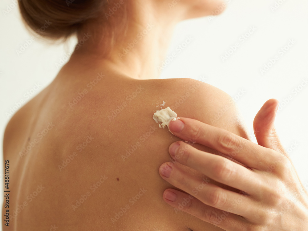 woman's shoulder with a hand spreading white body cream, on a white background, without a face woman's shoulder with a hand spreading white body cream, on a white background, without a face