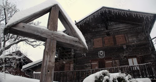 Croix chrétienne devant un vieux chalet de bois. Flocons de neige qui tombent doucement photo