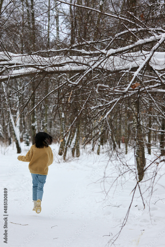 Moscow Russian Happy Running brunette girl in blue jeans white shoes and yellow jacket in winter park with white snow and trees cloudy weather Moscow Russian Happy Running brunette girl in blue jeans white shoes and yellow jacket in winter park with white snow and trees cloudy weather