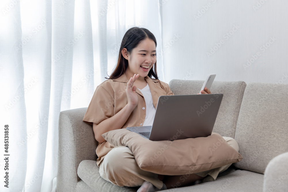 Asian woman talking on the phone and working on a laptop with a smiling face, Business Cell Phone Conversations, Working at home, Home lifestyle, Stay home, New normal, learning, Social distancing. Asian woman talking on the phone and working on a laptop with a smiling face, Business Cell Phone Conversations, Working at home, Home lifestyle, Stay home, New normal, learning, Social distancing.