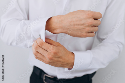 elegant young fashion man looking at his cufflinks while fixing them.