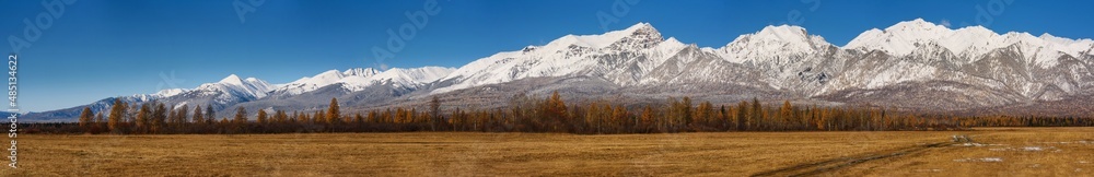 Panoramic autumn landscape. A field in the foreground and a forest and mountains in the distance. Mountain landscape. Panorama of nature. Mountainous terrain.