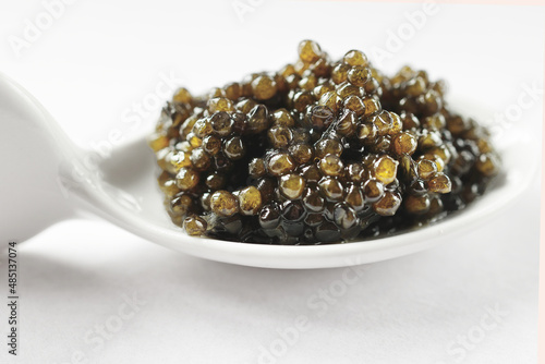 Natural black caviar in a white porcelain spoon on a white background. Product segment. Place for the inscription. Daylight.