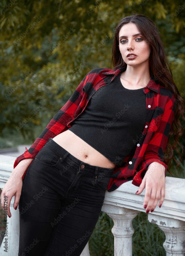 City fashion: portrait of cute young girl wearing checkered shirt, jeans  and topic in park Stock Photo