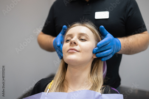 Doctor orthodontist-gnathologist palpates the jaw joints of the female patient photo