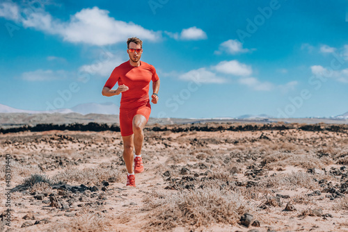 Runner ultra running man athlete wearing smartwatch, sunglasses, red compression clothes for trail run. Athlete training endurance race doing triathlon workout in desert photo