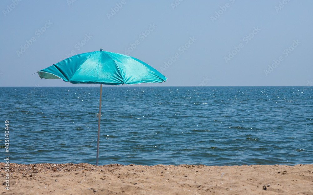 Beach umbrella with pale pink stripes in the foreground, against the blue sea background