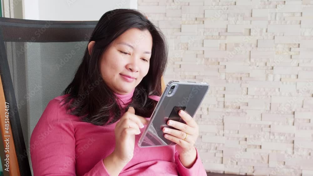 Close up Asian woman relaxing on a pool bed and using digital tablet near the private pool during her morning vacation. Close up Asian woman relaxing on a pool bed and using digital tablet near the private pool during her morning vacation.