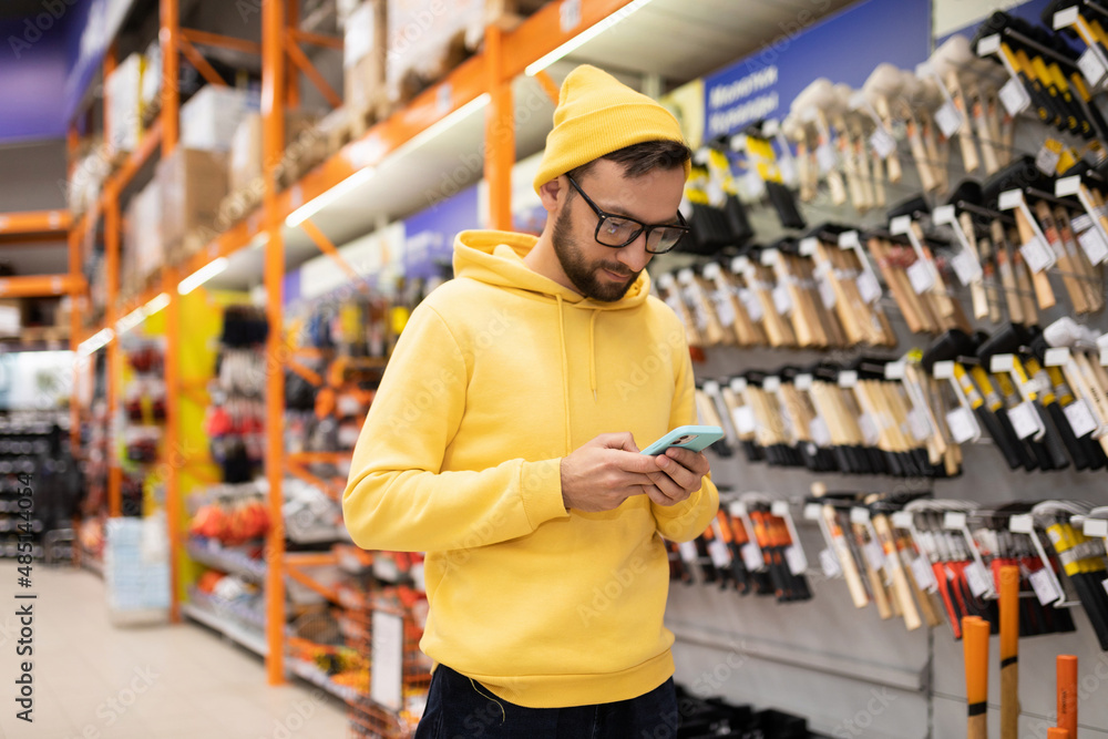 a young man with a phone in his hands in a hardware store next to a showcase with hammers a young man with a phone in his hands in a hardware store next to a showcase with hammers