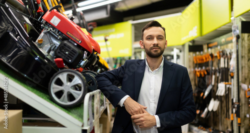 Fotografie sales manager in a gardening equipment store next to a petrol lawn mower