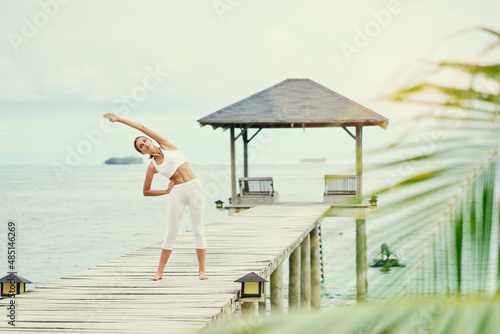 Fitness on the beach. Young woman exercising on wooden pier with sea view.