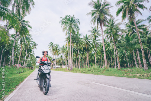 Tropical travel and transport. Young beautiful woman in helmet riding scooter on the road with palm trees.