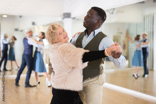 Fototapeta Elderly woman learning ballroom dancing in pair in dance studio
