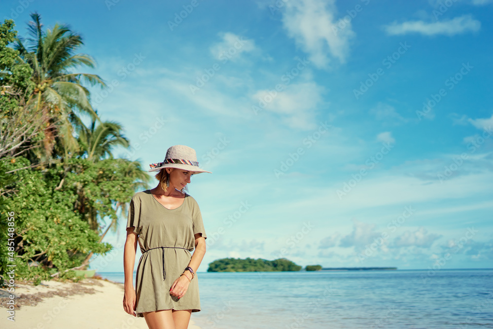 Vacation on the seashore. Young woman in hat on the beautiful tropical white sand beach.