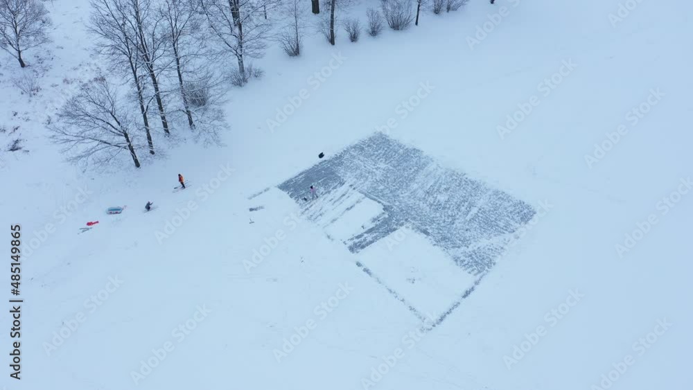 Aerial view of a frozen pond in winter, people clean the ice from the snow with a large shovel for skating, a winter ice rink Aerial view of a frozen pond in winter, people clean the ice from the snow with a large shovel for skating, a winter ice rink