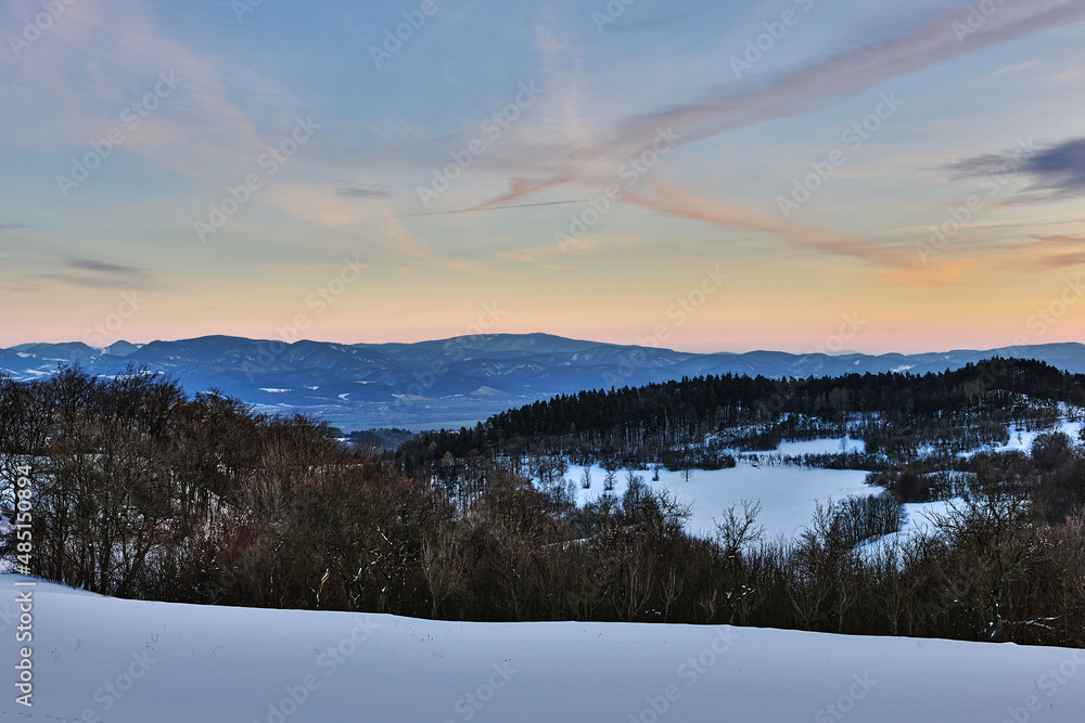 Winter snowy mountain landscape at dusk. Shortly after sunset. With forest and hills. Sky in blue oange. Nature background, wallpaper. Protected area Vrsatec, Slovakia.