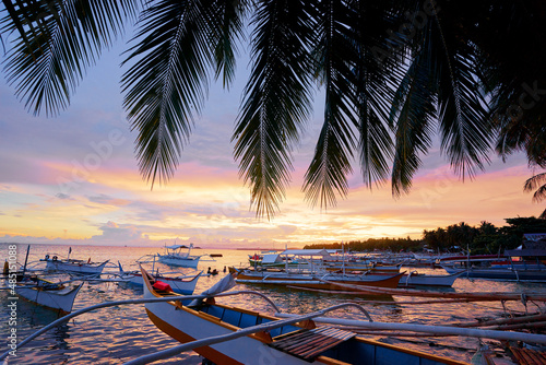 Beautiful colorful sunset on the seashore with fishing boats and palm leaves. Philippines, Siargao Island.