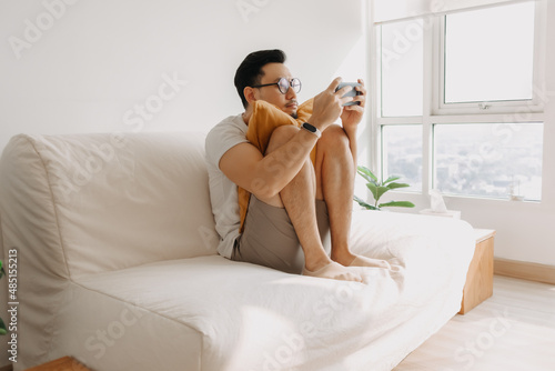 Adult Asian man is having fun to play mobile game in the living room apartment.