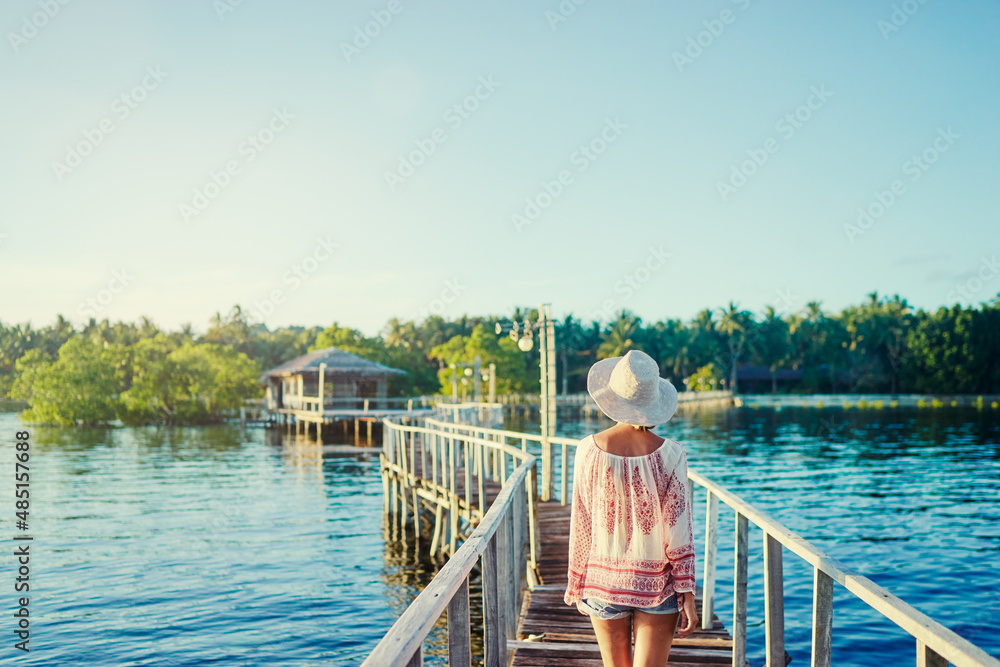 Fototapeta premium Vacation on tropical island. Back view of young woman in hat enjoying sea view from wooden bridge terrace, Siargao Philippines