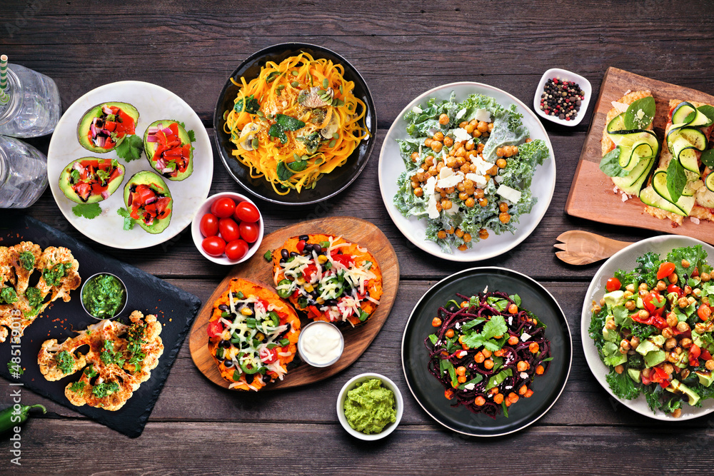 Healthy plant based, low carb diet table scene. Above view on a dark wood background. Vegetable noodles, cauliflower flatbread and steaks, kale salads, stuffed avocados and sweet potatoes. Healthy plant based, low carb diet table scene. Above view on a dark wood background. Vegetable noodles, cauliflower flatbread and steaks, kale salads, stuffed avocados and sweet potatoes.