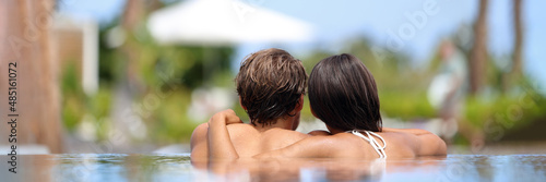 Luxury spa couple relaxing at pool resort hot tub panoramic view from behind of two people. Adults only hotel travel vacation getaway for honeymoon. Woman and man hugging