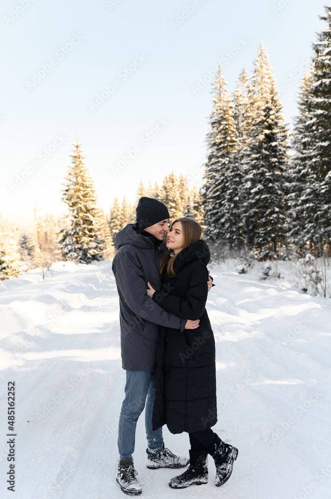 young couple in love hugging on a snowy road surrounded by forest. winter family walks. young couple in love hugging on a snowy road surrounded by forest. winter family walks.
