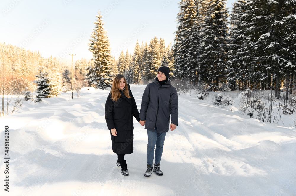 young couple in love hugging on a snowy road surrounded by forest. winter family walks.