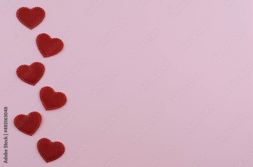 Vertical ornament of red velvet hearts on a light pink background. Minimalism.