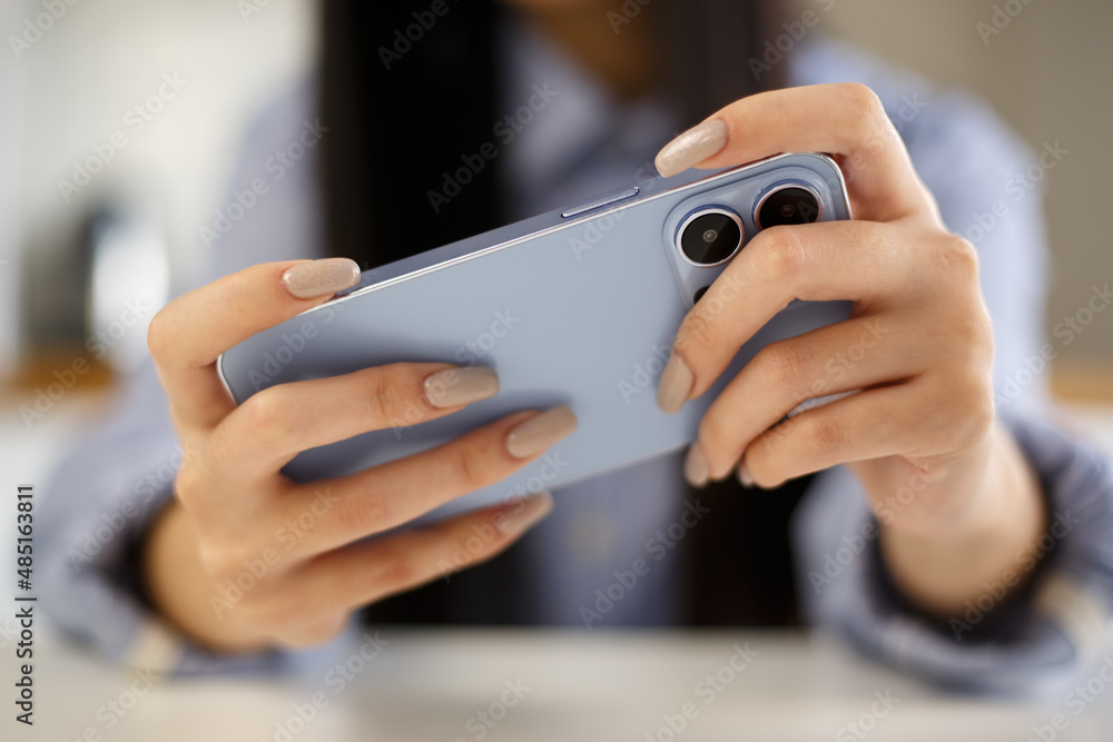 Gamer girl playing mobile games on smartphone. Young adult female using modern blue mobile phone to play video game app at home. Gamer girl playing mobile games on smartphone. Young adult female using modern blue mobile phone to play video game app at home.