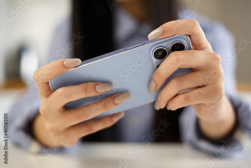 Gamer girl playing mobile games on smartphone. Young adult female using modern blue mobile phone to play video game app at home.