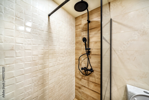 Modern shower zone with black rain head, hand held shower and glass door. Light beige and wood patern tiles in the bathroom.