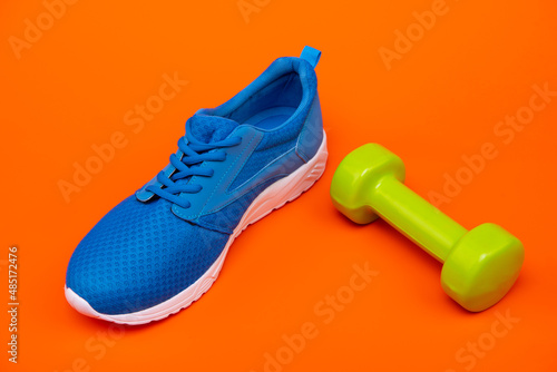sporty blue sneaker with barbell on orange background, sport accessory