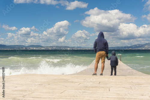 Father and son are standing on the pier, admiring the seascape, raging autumn sea.