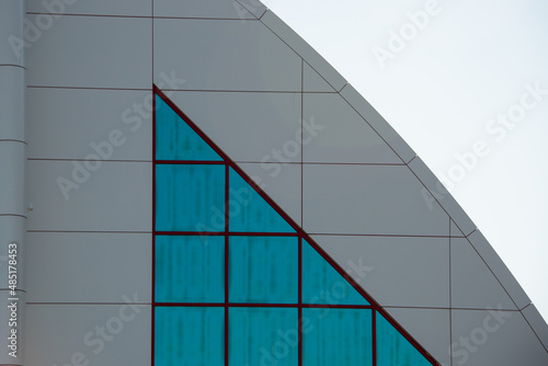 The exterior wall of a contemporary commercial style building with aluminum metal composite panels and glass windows. The futuristic building has engineered diagonal cladding steel frame panels.