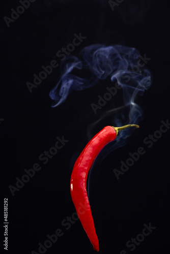 Red hot chili peppers against a black background with smoke coming from it, depicting it to be smoking hot. High quality photo
